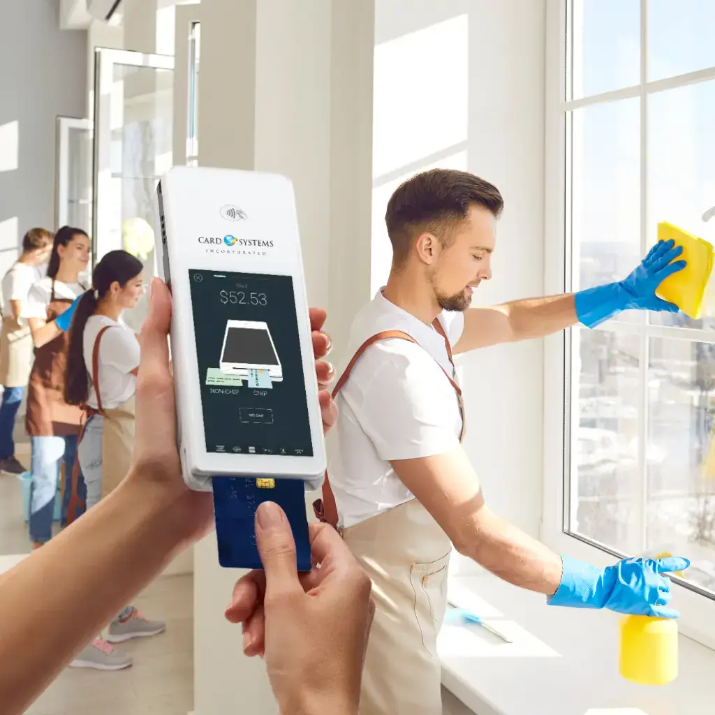 Mobile point-of-sale (POS) device being used to process a payment for a cleaning service in the field, with cleaners working in the background.