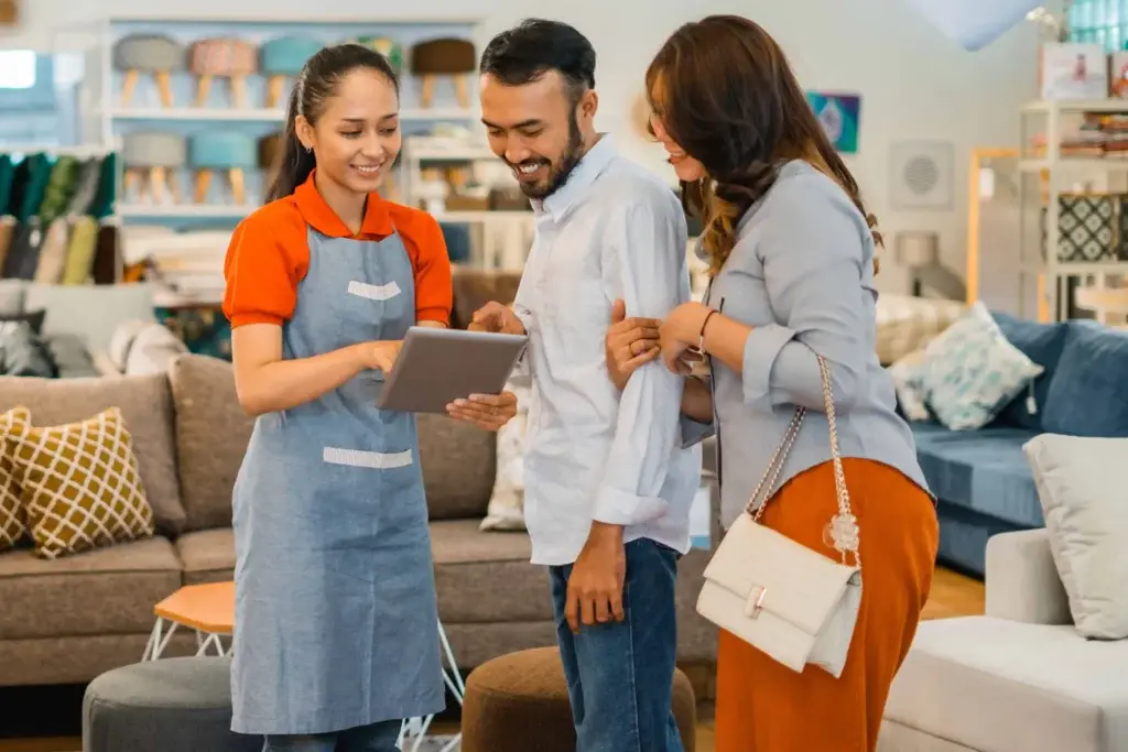 Sales assistant using a tablet POS system to assist a smiling couple in a furniture store.
