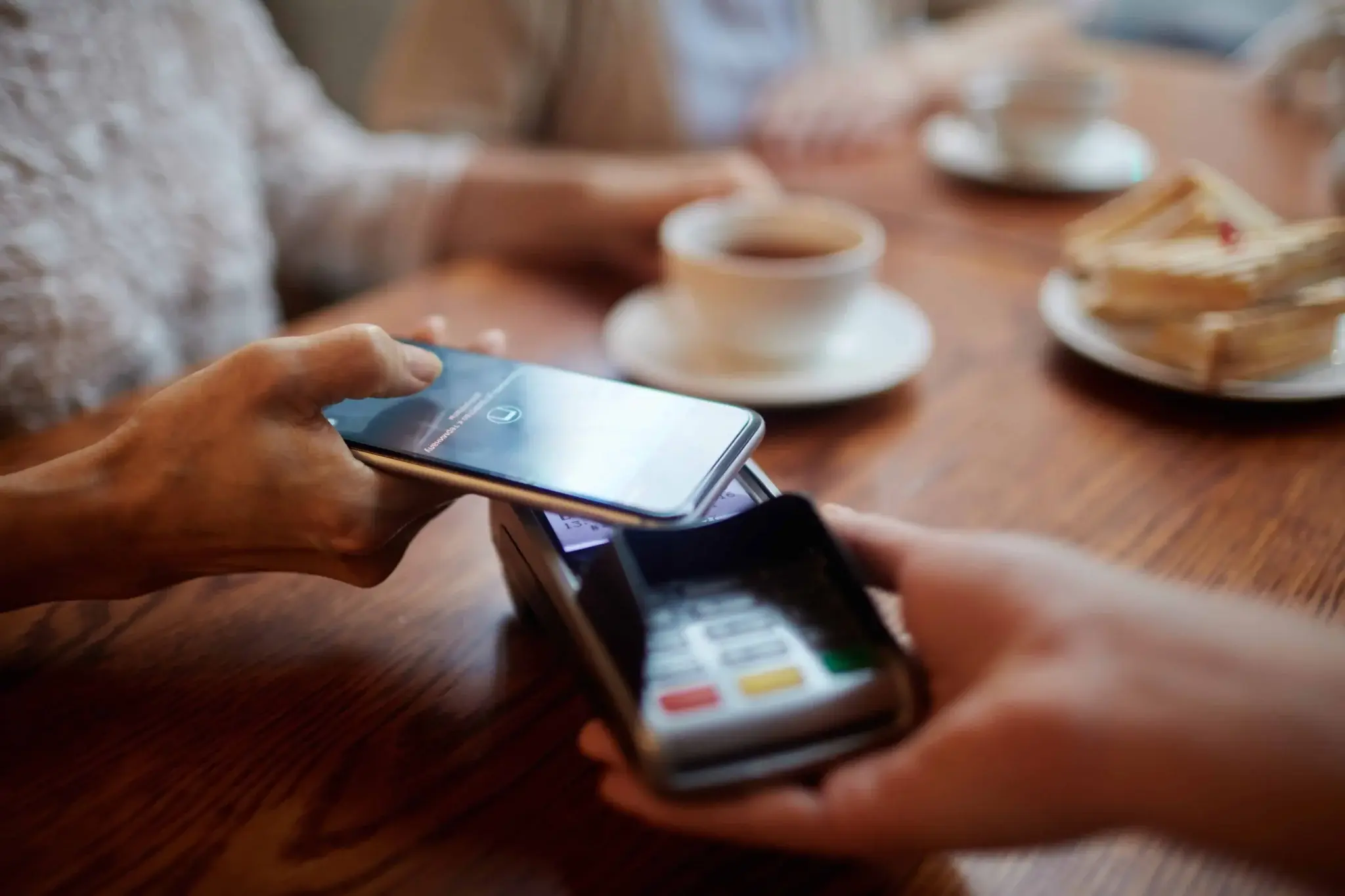 A restaurant guest using a smartphone for contactless payment with a modern POS system at the table.